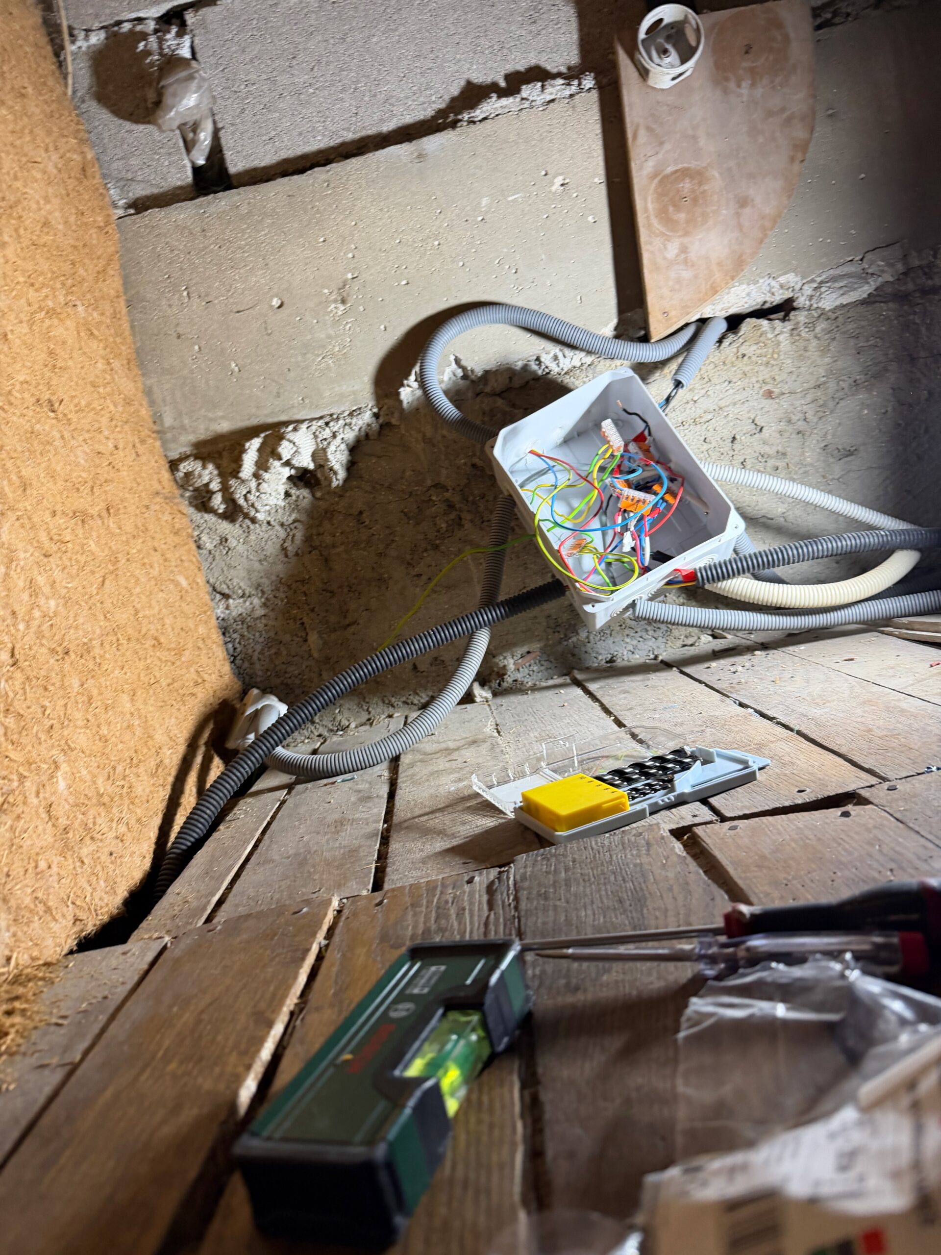Sous-pente de toit avec gaines électriques, boîtier de dérivation posé au sol et outils de contrôle électrique.