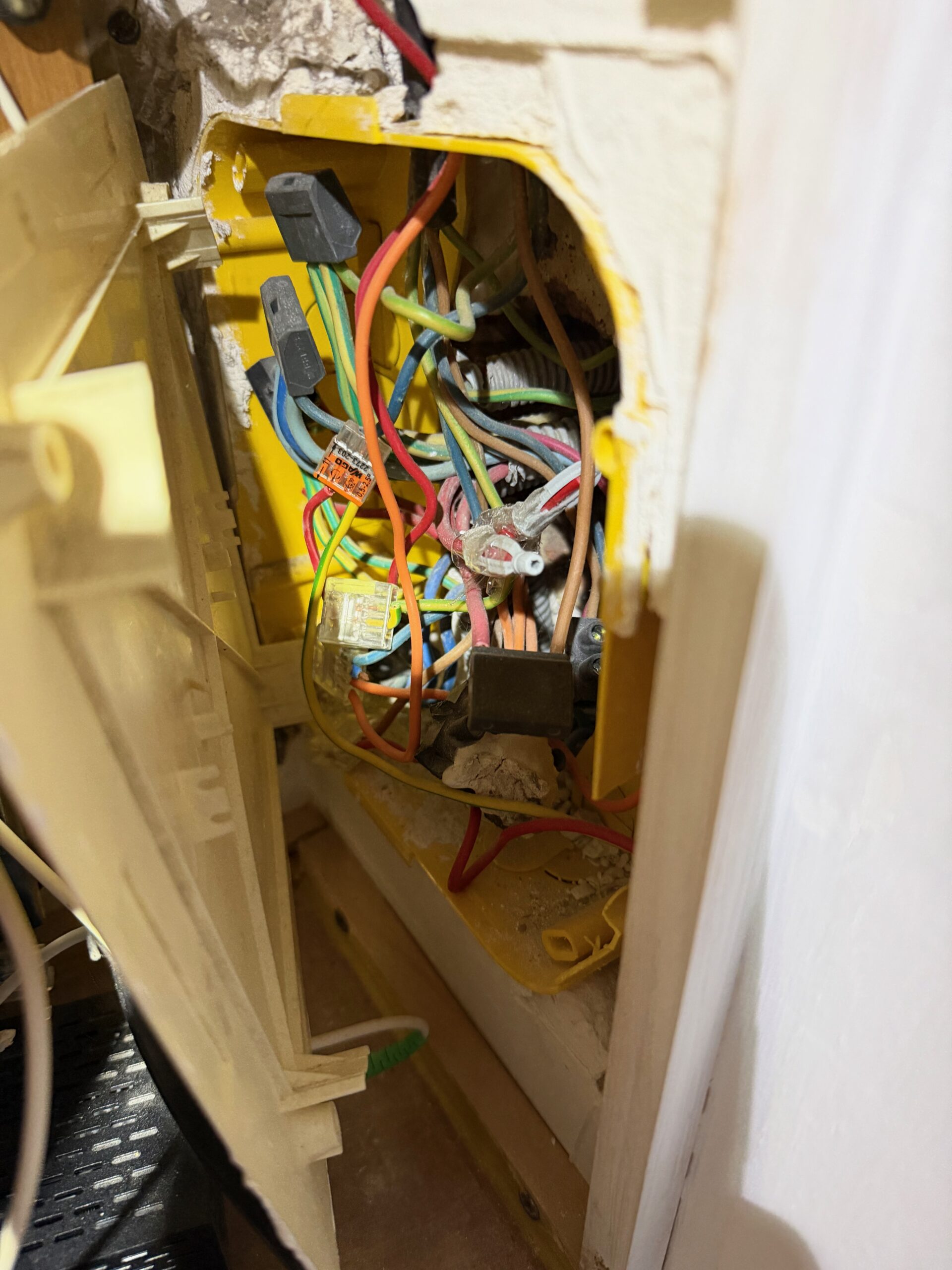 Boîtier électrique encastré dans un mur jaune avec plusieurs câbles multicolores emmêlés.