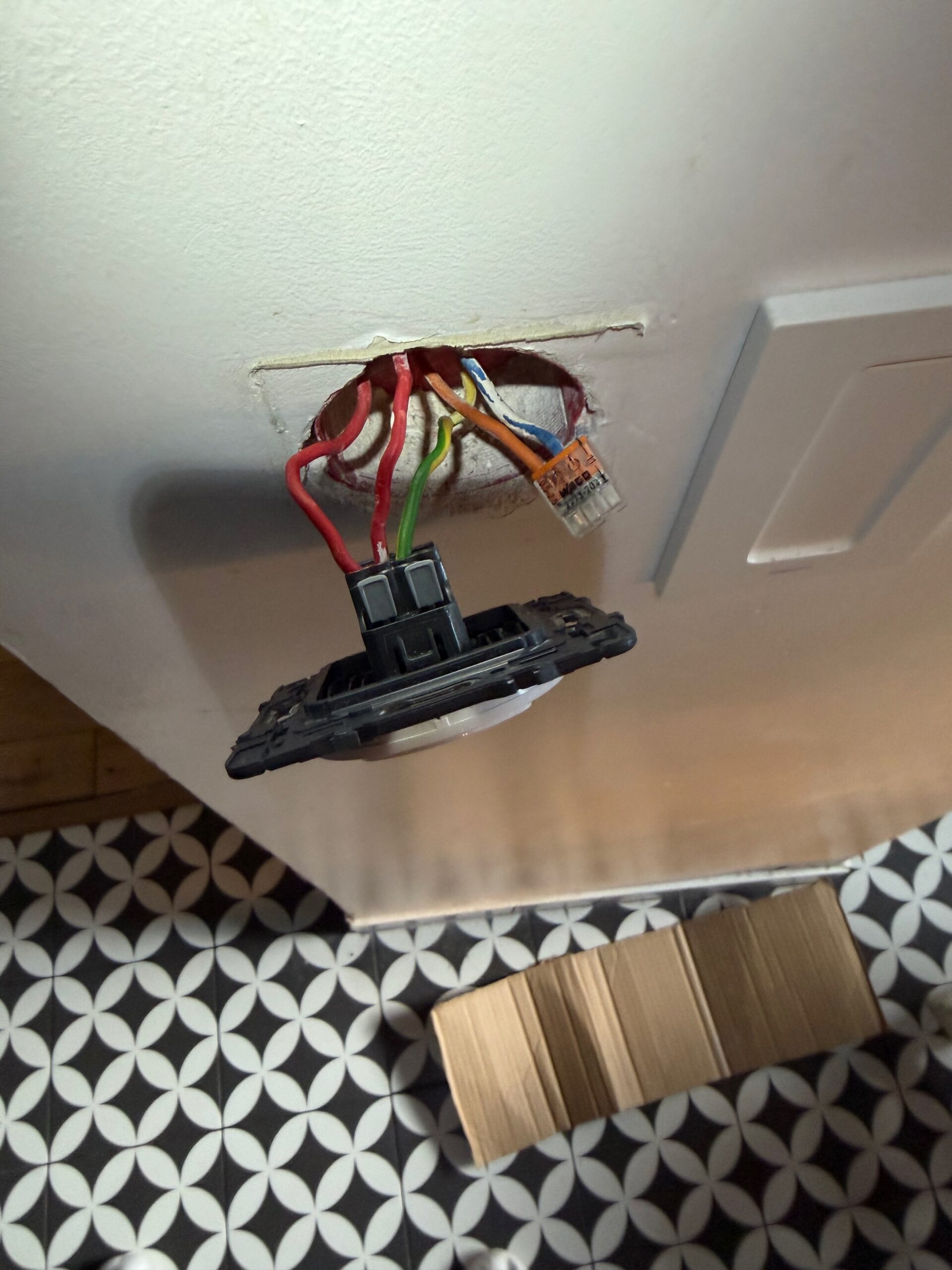 Fils électriques reconnectés avec un connecteur Wago au plafond d'une salle de bain, prêts pour la pose du luminaire.