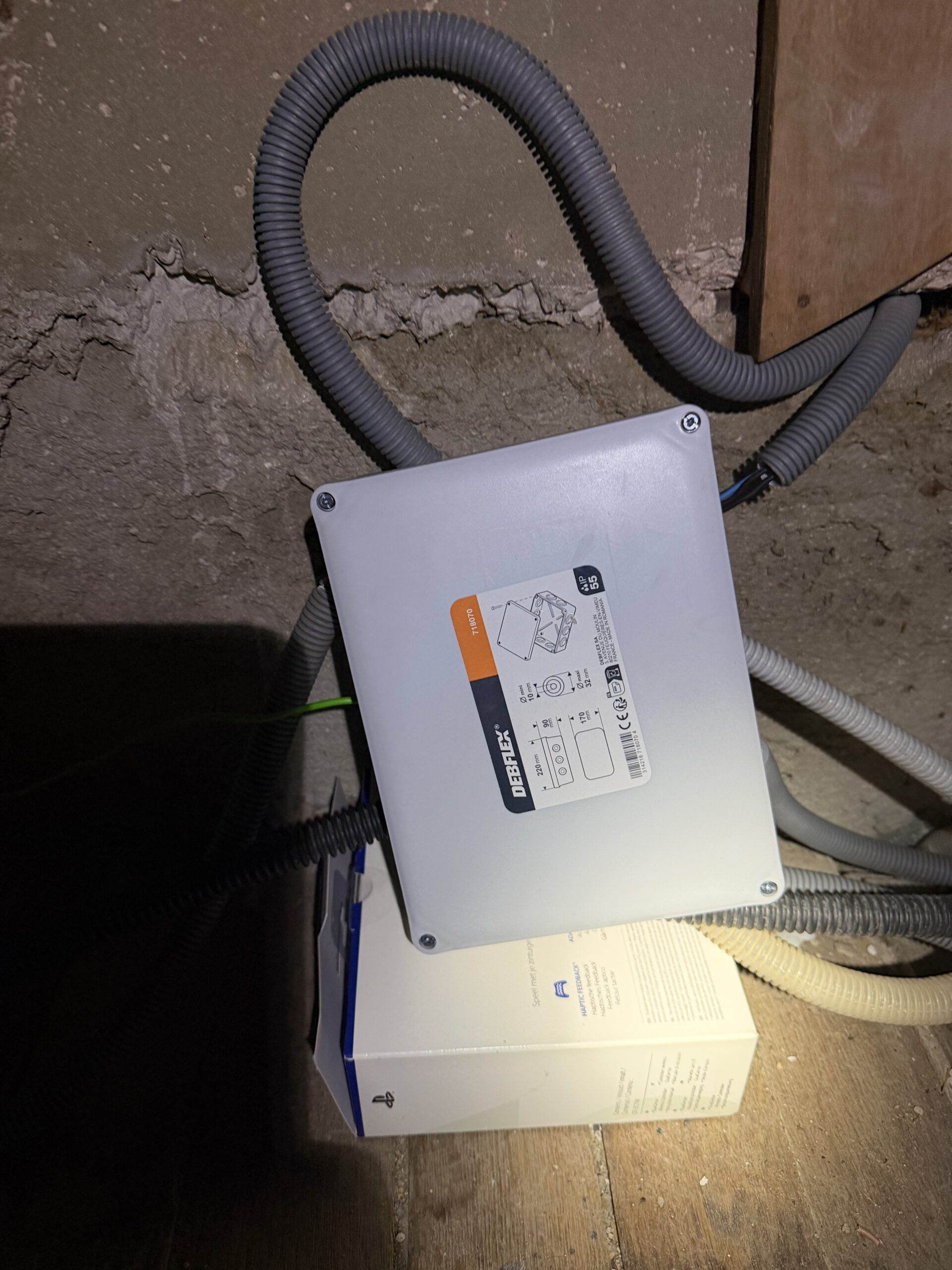 Boîtier de dérivation électrique fixé au mur dans une sous-pente, gaines électriques raccordées.