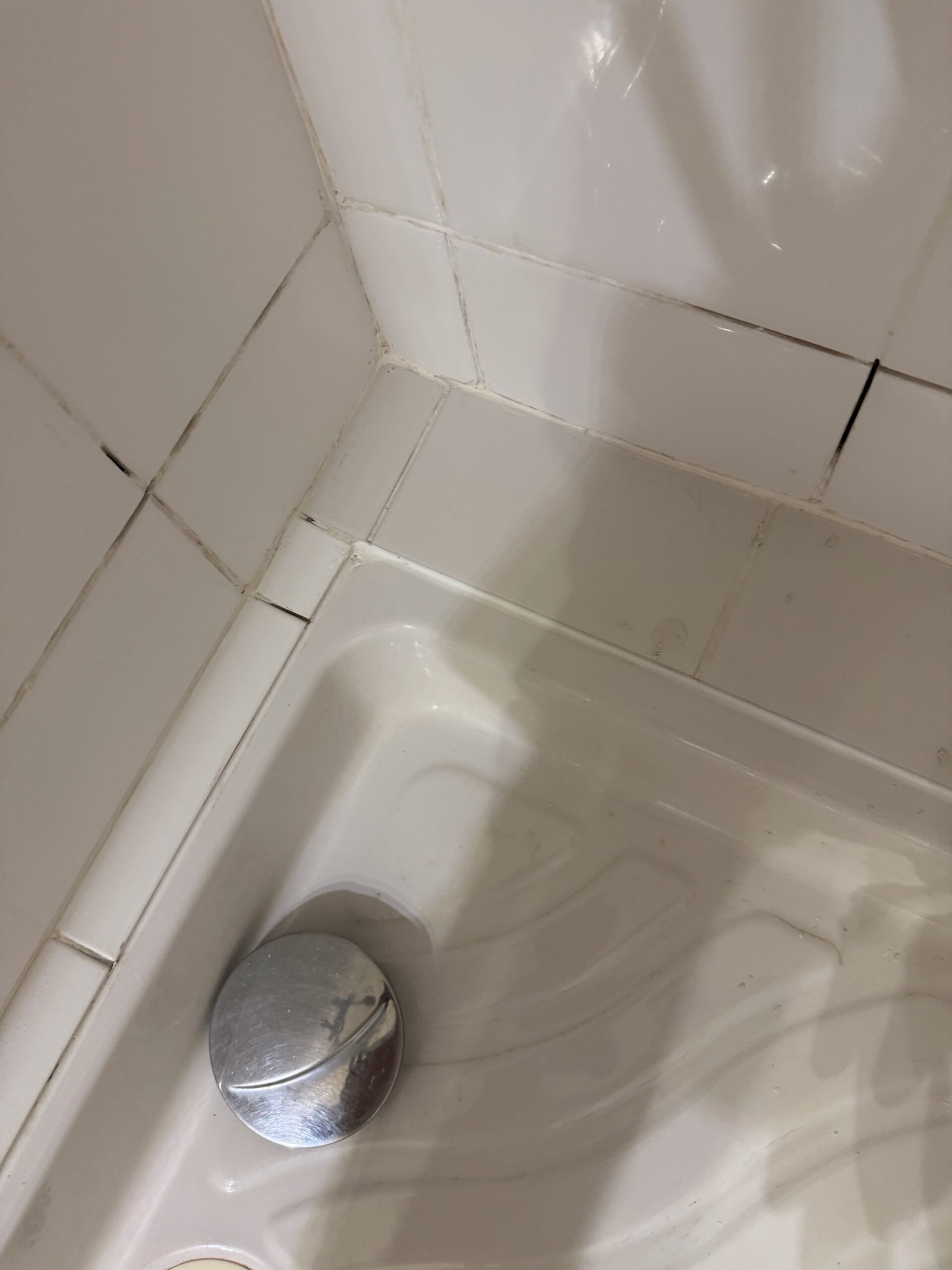 Joints de carrelage fissurés et joint silicone abîmé autour du bac de douche, avant intervention
